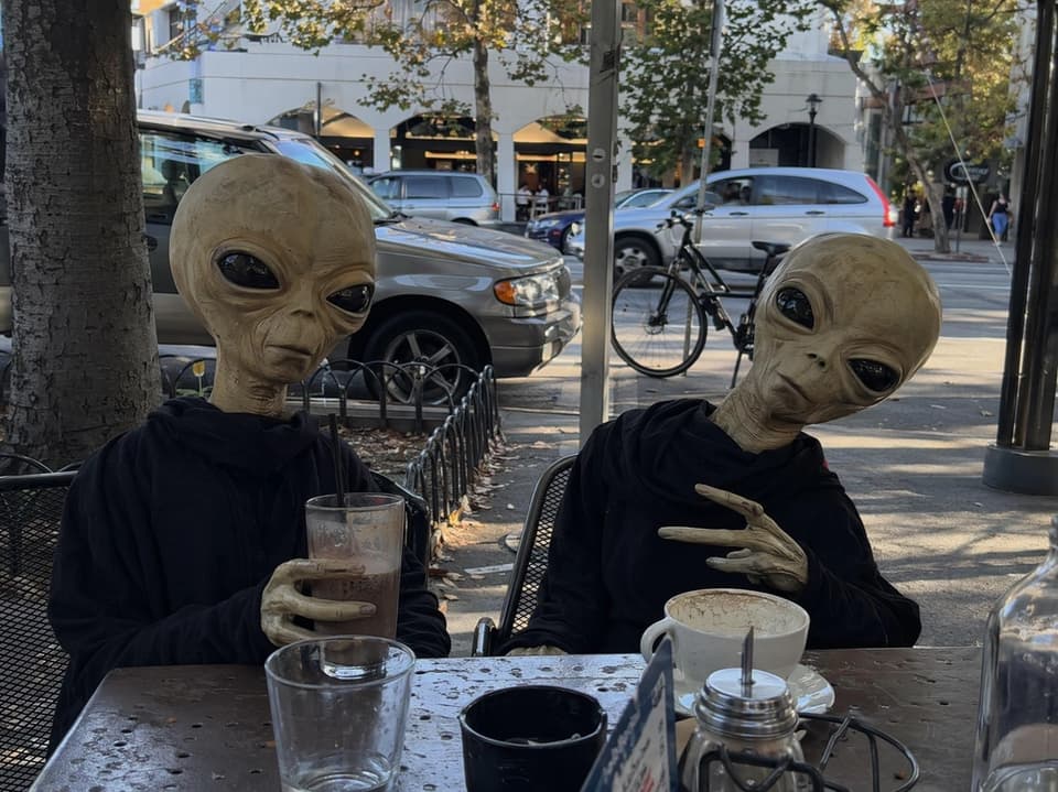 GPT Image 2 official sample — photorealistic phone snapshot of two aliens at an outdoor cafe, casual everyday realism